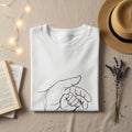 White t-shirt with simple line drawing of adult and baby hands.