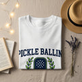 White t-shirt with "PICKLE BALLIN" text and pickleball paddle graphic.