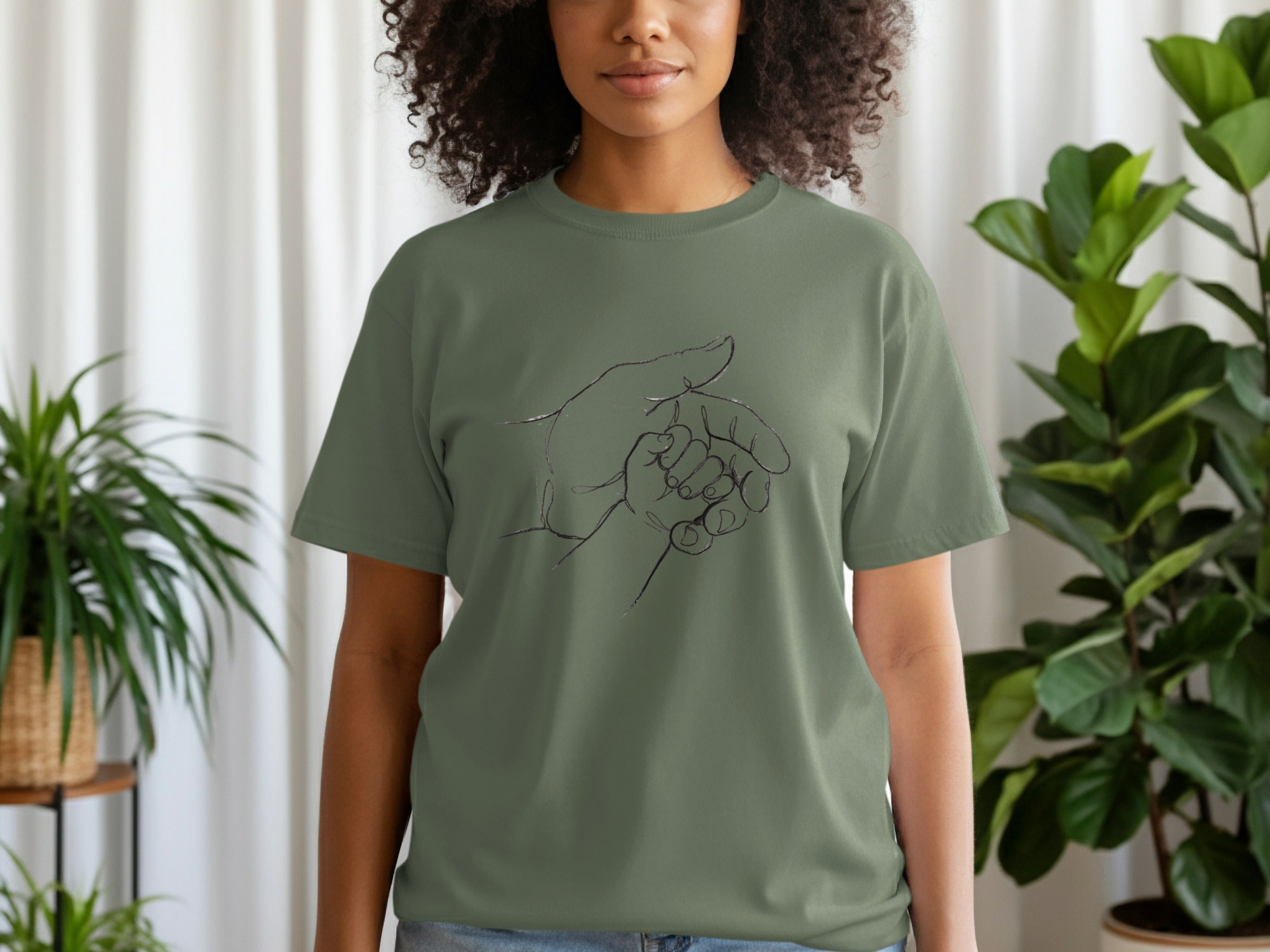 Olive green t-shirt with a black line drawing of a parent's hand holding a child's hand.