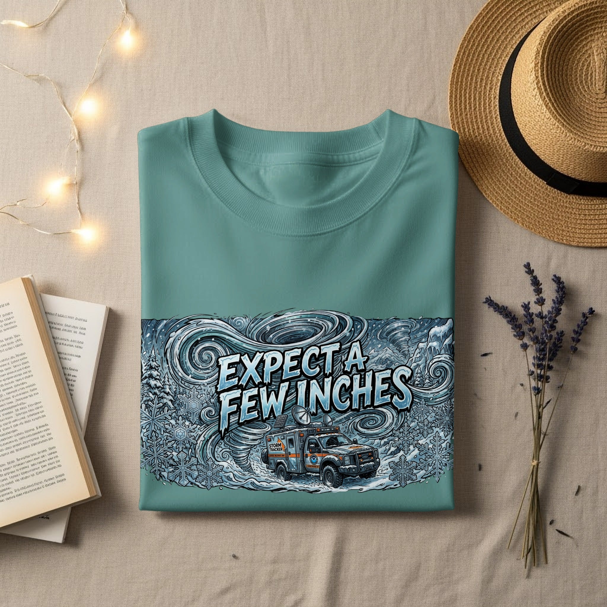 Teal t-shirt with "EXPECT A FEW INCHES" graphic featuring a snowstorm and storm tracker vehicle.