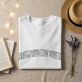 White sweatshirt with "PROMPTED NOT CODER" text, straw hat, and book.