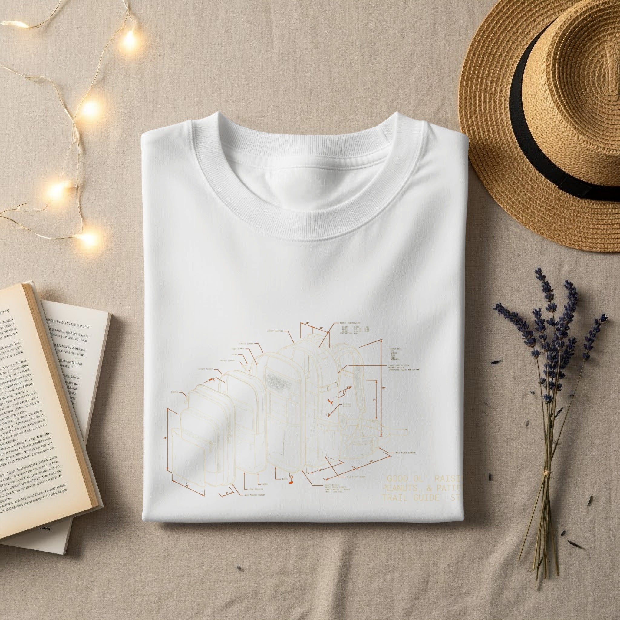 White t-shirt with diagram of a backpack and text, laid flat with hat and book.