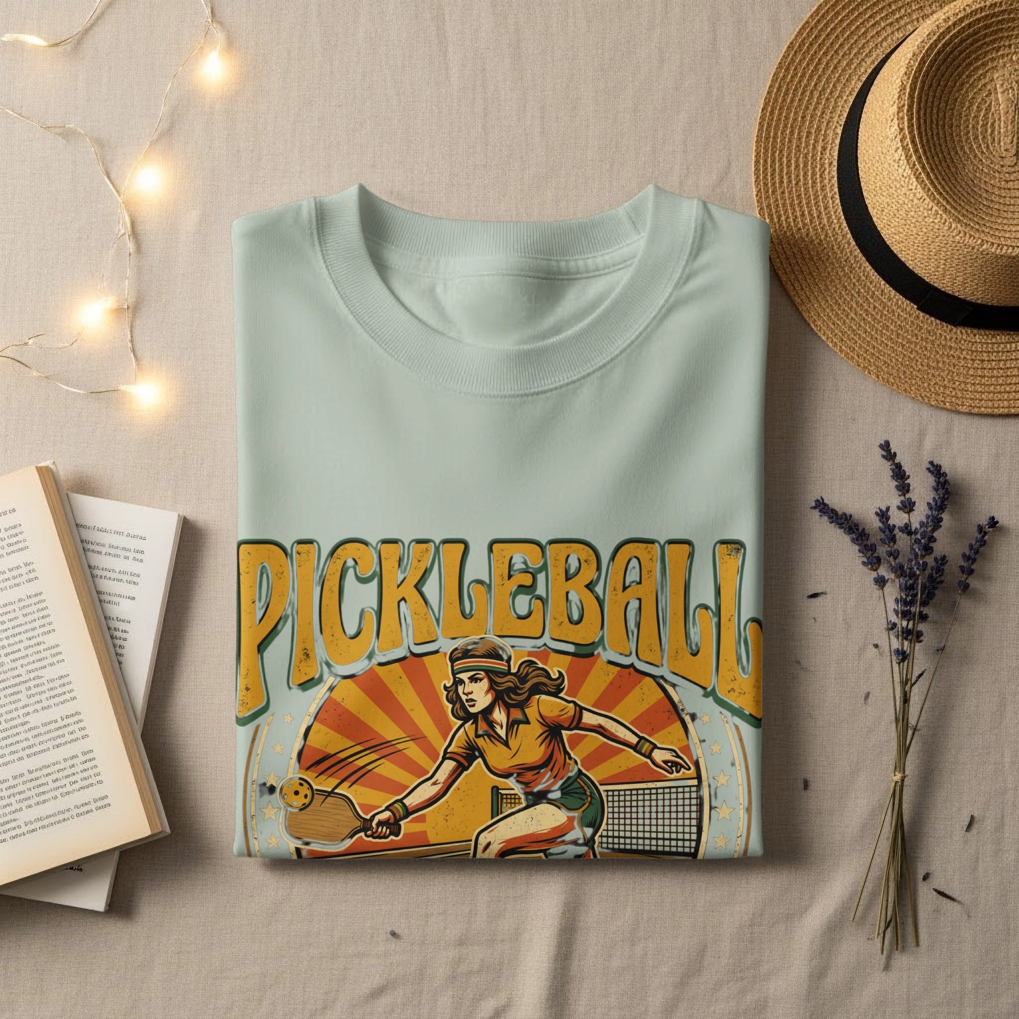 Light teal t-shirt with "PICKLEBALL" text and graphic of a woman playing.