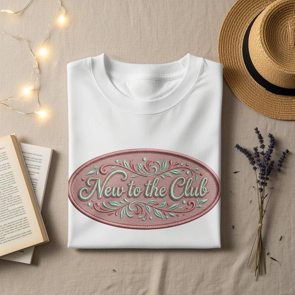 White t-shirt with oval "New to the Club" embroidery, hat, and book.