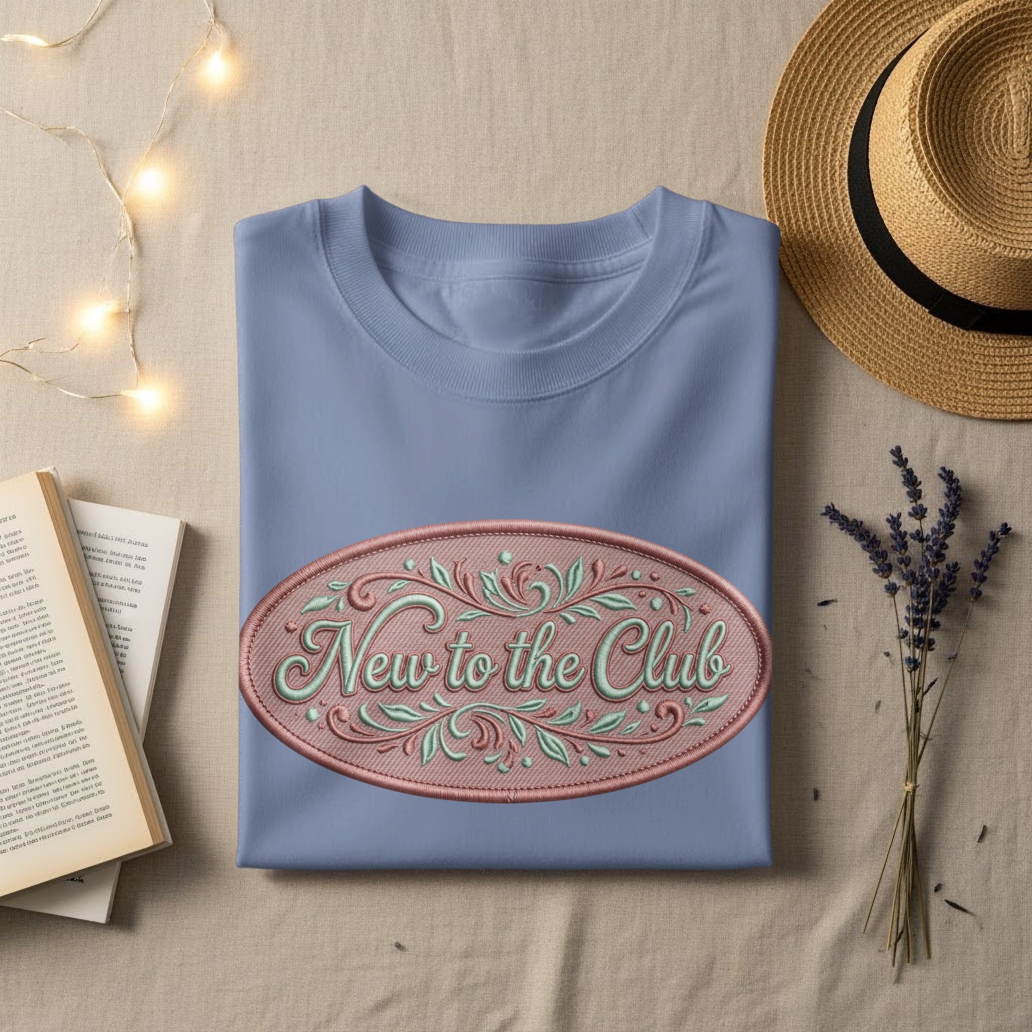 Light blue t-shirt with "New to the Club" embroidered in a decorative oval.