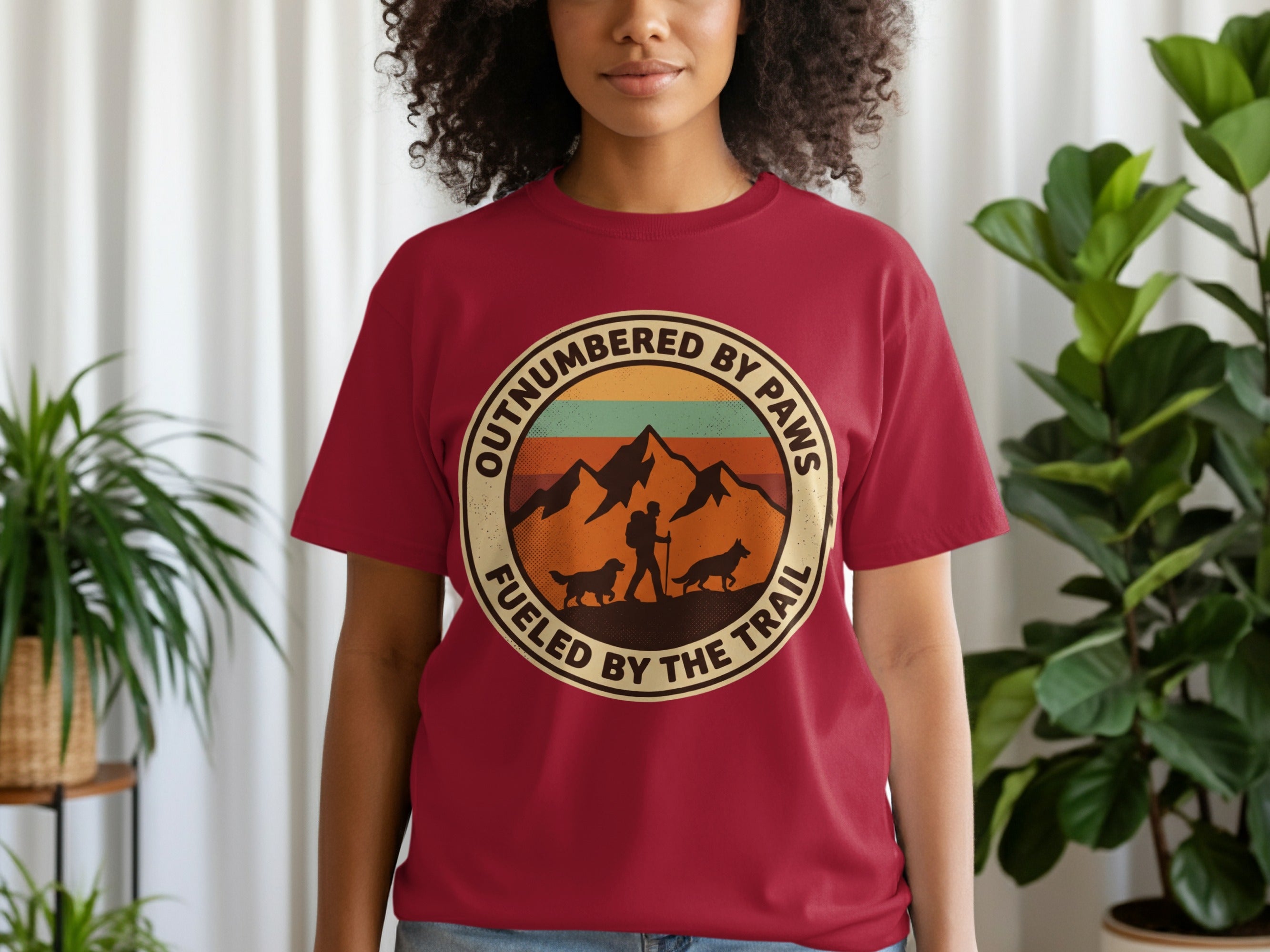 Maroon t-shirt with circular graphic: mountains, dogs, hiker, and text "Outnumbered by Paws Fueled by the Trail".