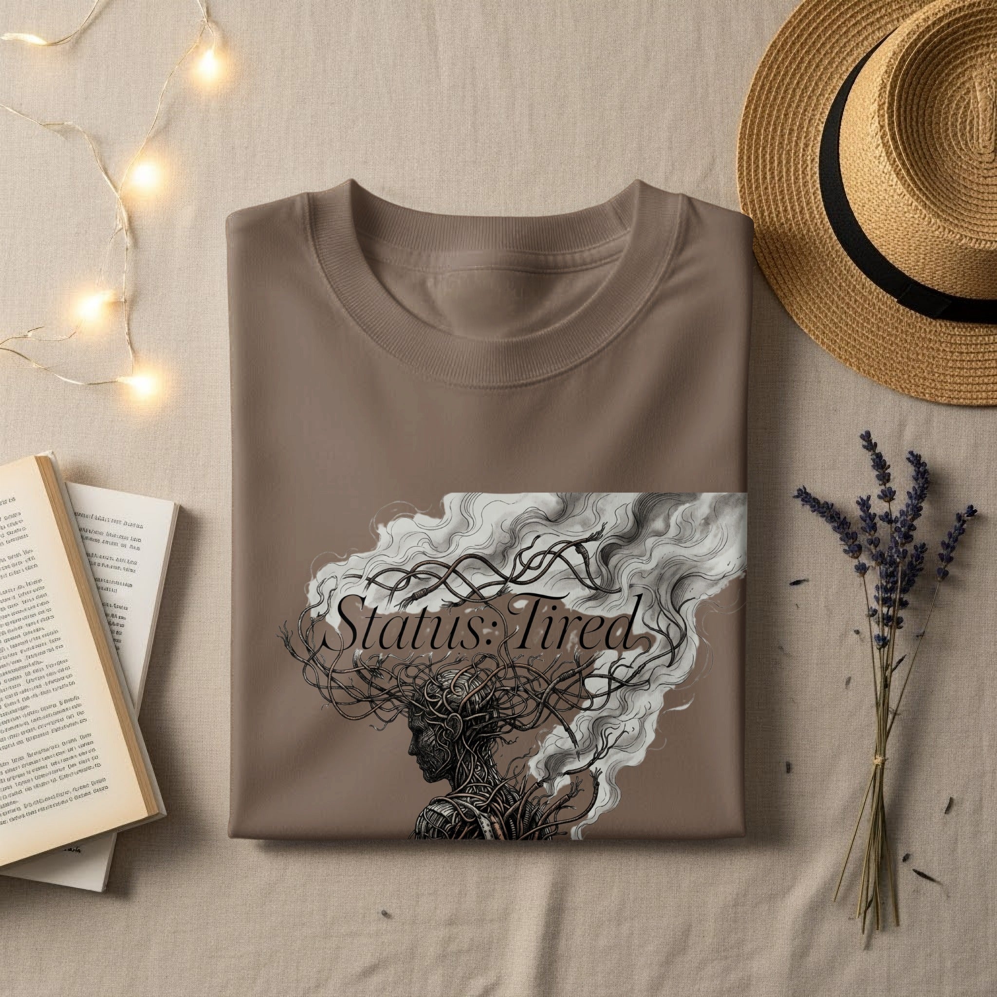 Brown t-shirt with "Status: Tired" text and artistic illustration of a head with swirling hair.