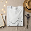 White t-shirt with abstract line art design, flat lay with straw hat and books.