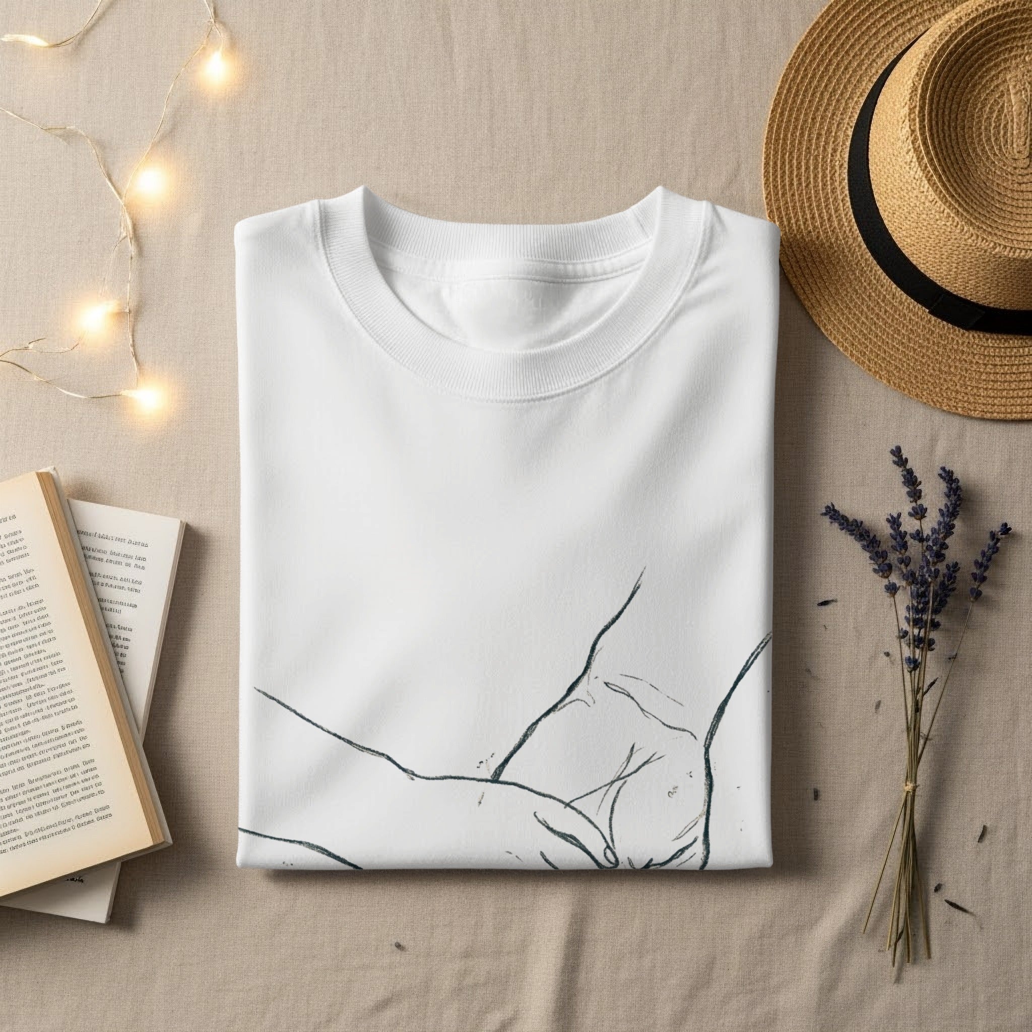 White t-shirt with abstract line art design, flat lay with straw hat and books.