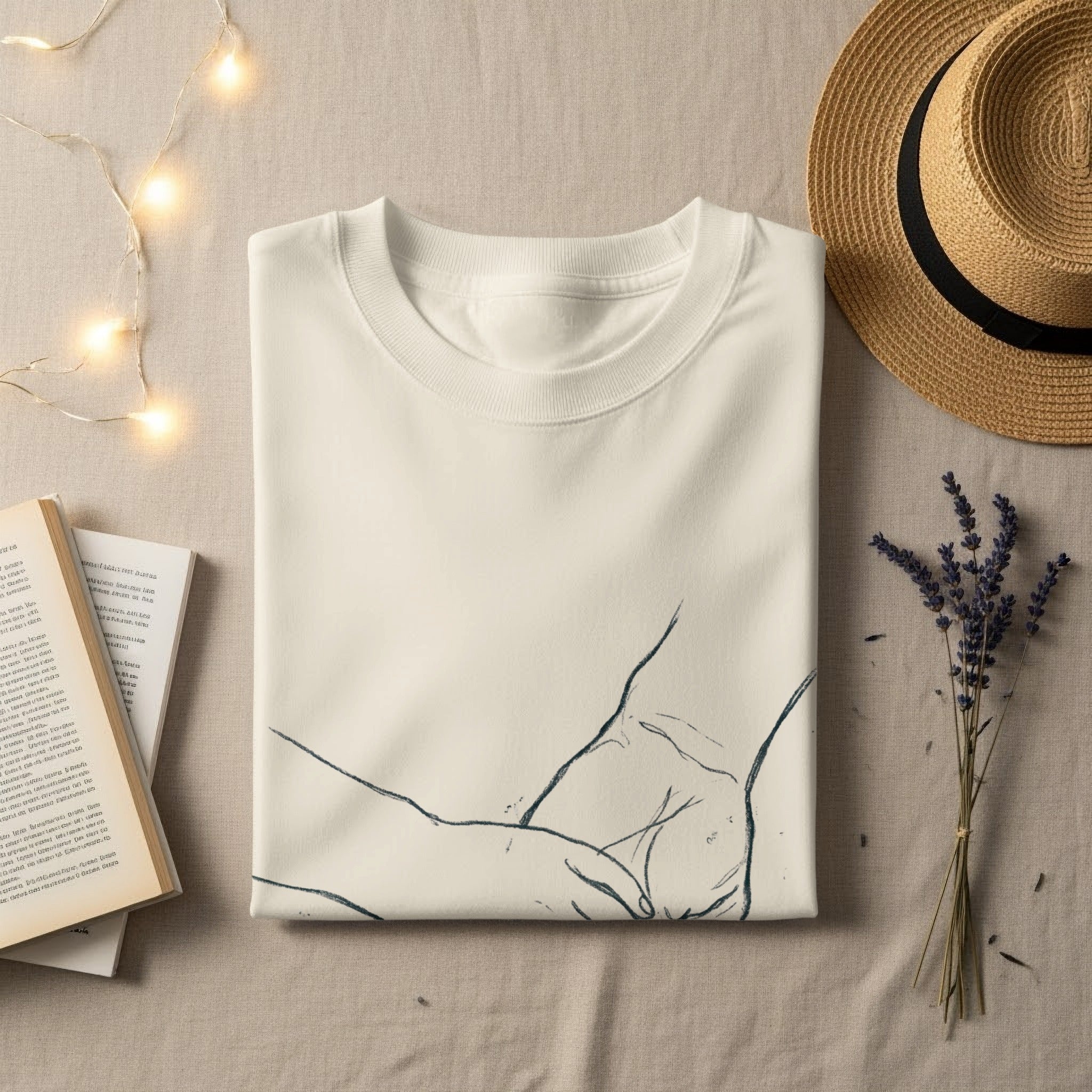 Cream t-shirt with minimalist line art of hands, straw hat, and book.