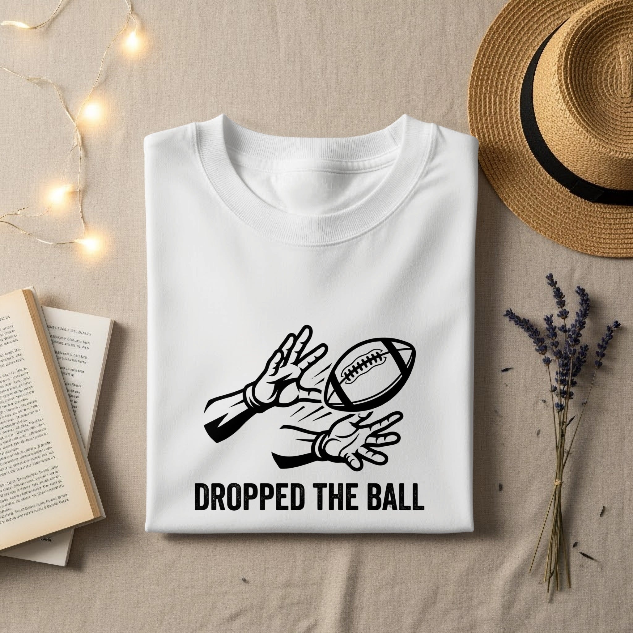 White t-shirt with "DROPPED THE BALL" text and graphic of hands reaching for a football.