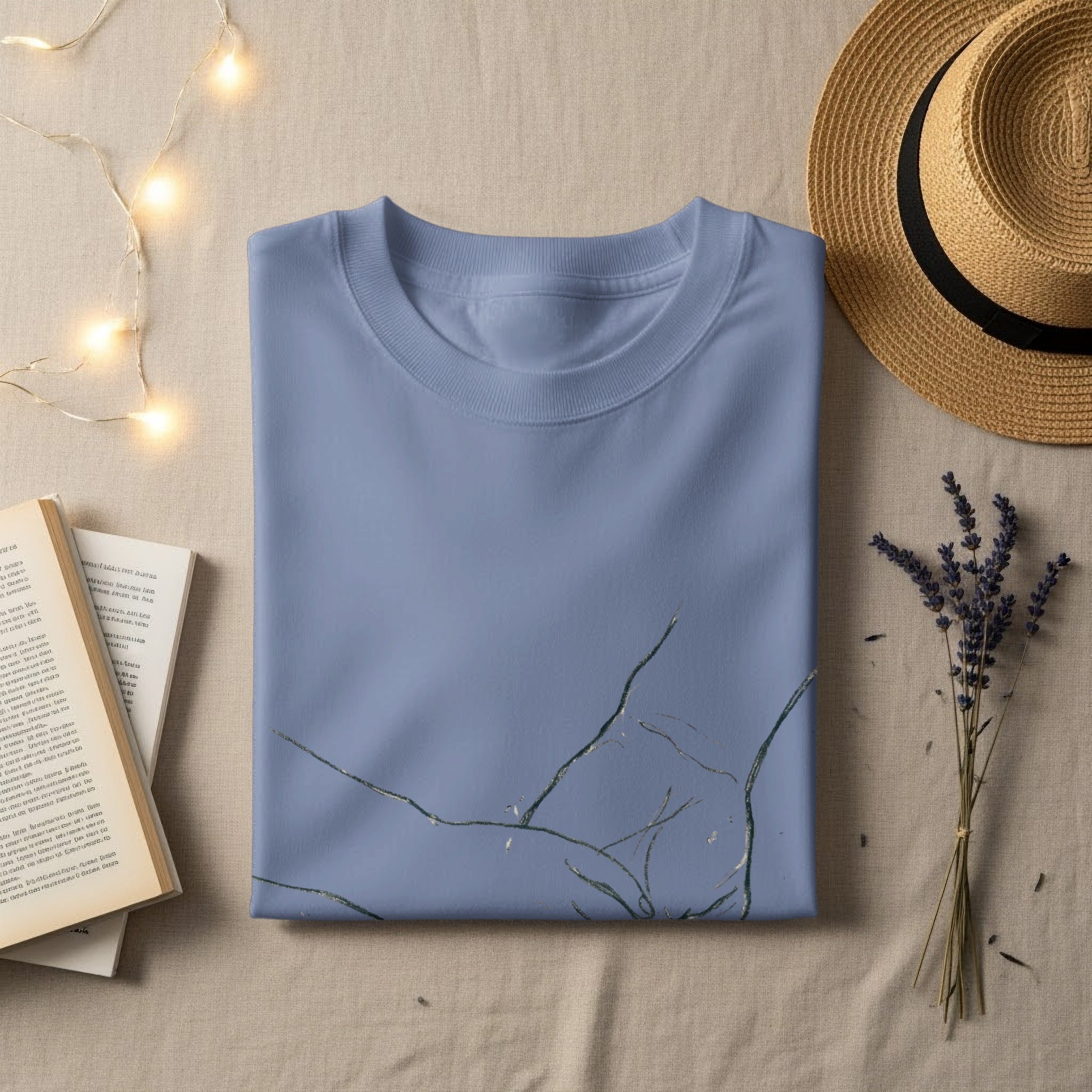 Blue t-shirt with a cracked gold foil design, lying flat with a straw hat and book.