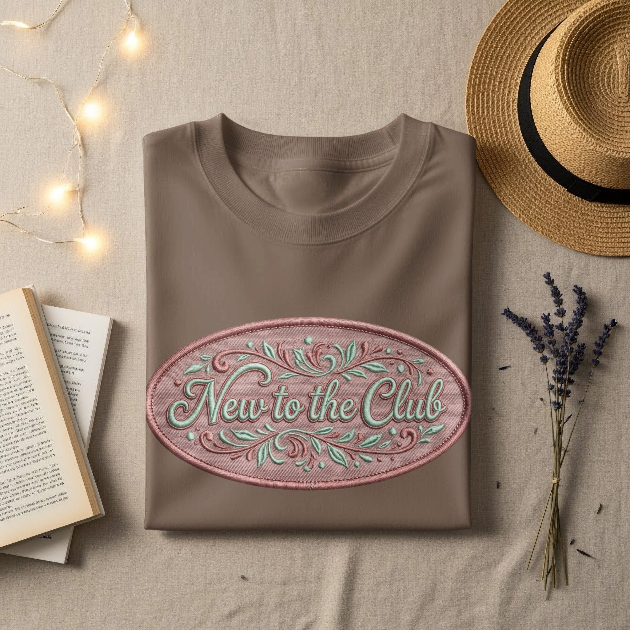 Brown t-shirt with embroidered oval logo reading "New to the Club".