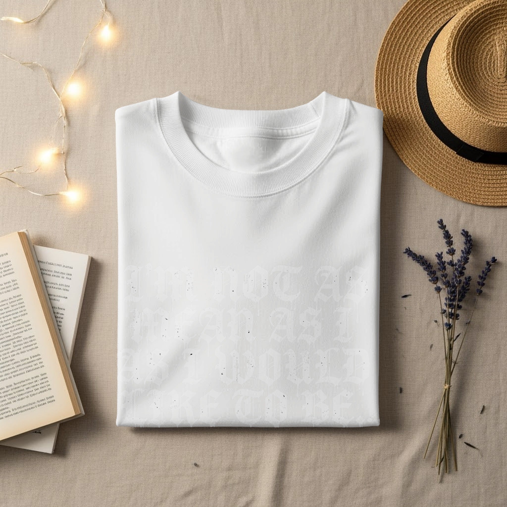 White t-shirt with "I'm not as mean as I would" text, flat lay with books and hat.