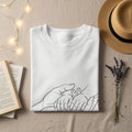 White t-shirt with minimalist line drawing of adult and baby hands.