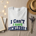 White t-shirt with "I Can't I HAVE DICKLEBALL" text, with hat and flowers.