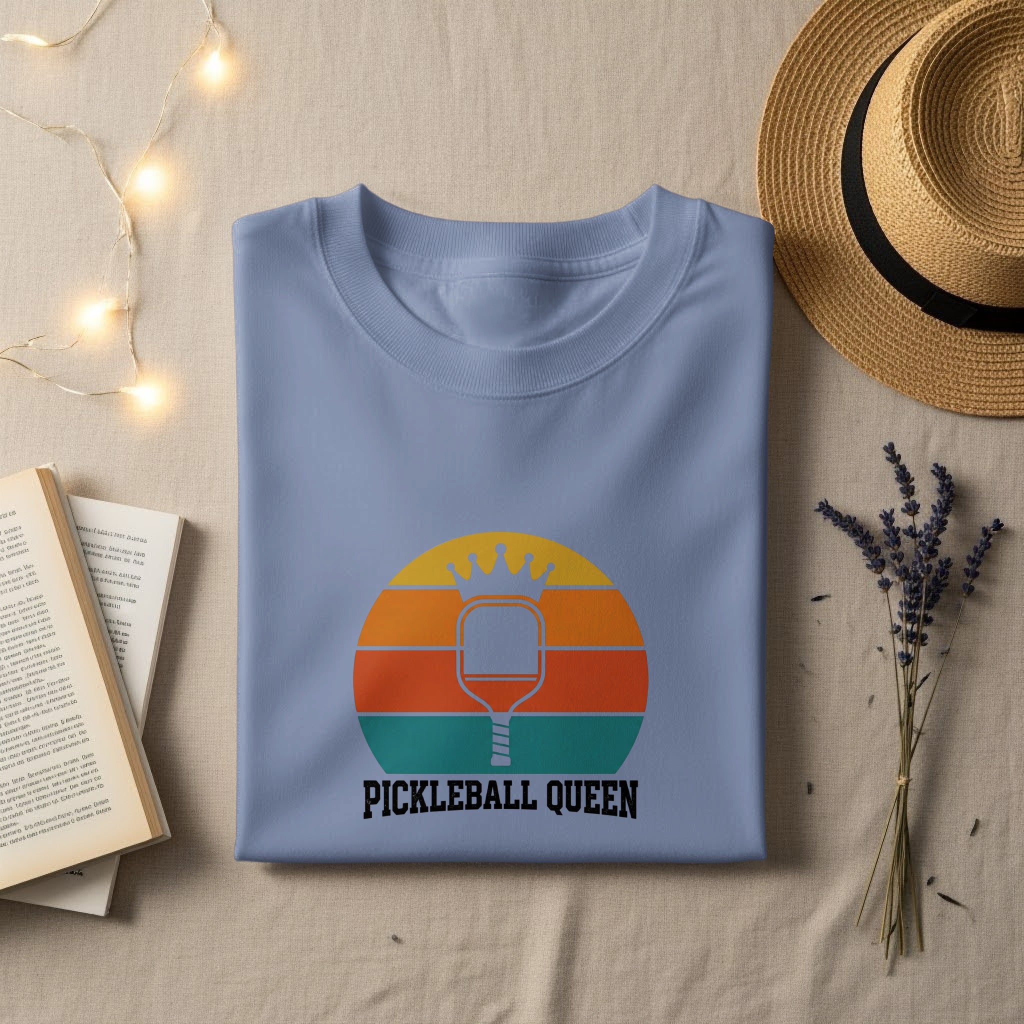 Light blue t-shirt with "PICKLEBALL QUEEN" and a pickleball paddle in a sunset circle.
