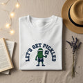 White t-shirt with "Let's Get Pickled" graphic of a pickle character.